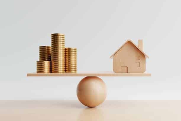 Balance en bois avec une maquette de maison et des pièces de monnaie illustrant la valorisation immobilière