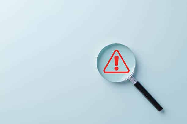 Loupe examinant un symbole d’avertissement rouge pour illustrer la vigilance avant des travaux