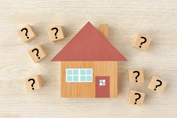 Maison en bois entourée de cubes avec des points d'interrogation illustrant une FAQ sur les travaux de rénovation à Andrézieux-Bouthéon.