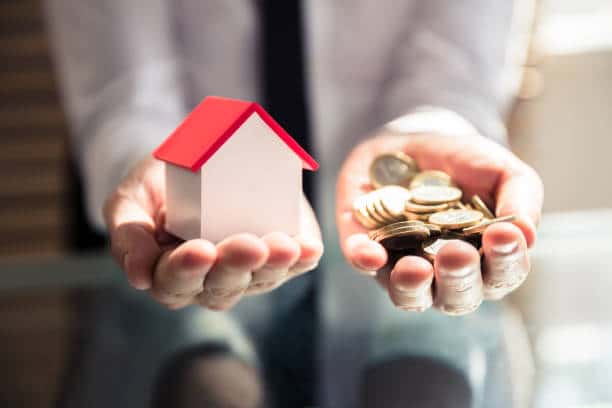 Mains tenant une maquette de maison et des pièces de monnaie pour illustrer l’estimation d’un projet de travaux