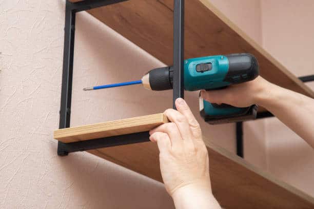 Personne fixant une étagère au mur avec une perceuse